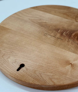 A close-up of a round wood serving board with visible wood grain, a small keyhole cutout for hanging board as decor.